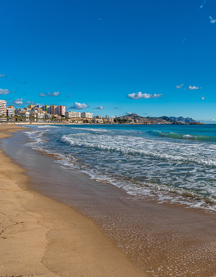 Vista del Mar Mediterráneo desde la arena de Cala Finestrat, con algunos edificios al fondo